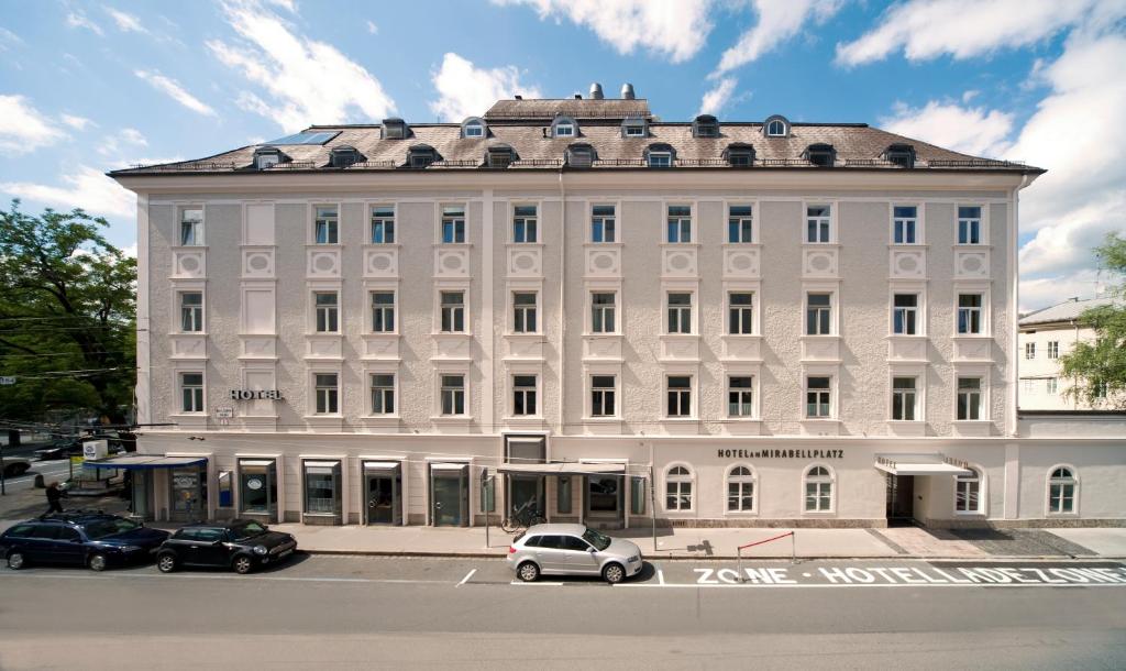 萨尔茨堡米拉贝尔广场奥斯超泰尔酒店的一座白色的建筑,前面有汽车停放