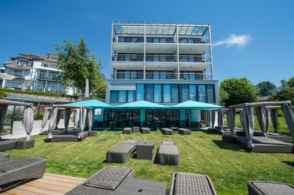 沃尔特湖畔韦尔登Boutiquehotel Wörthersee - Serviced Apartments的草丛中带椅子和遮阳伞的建筑