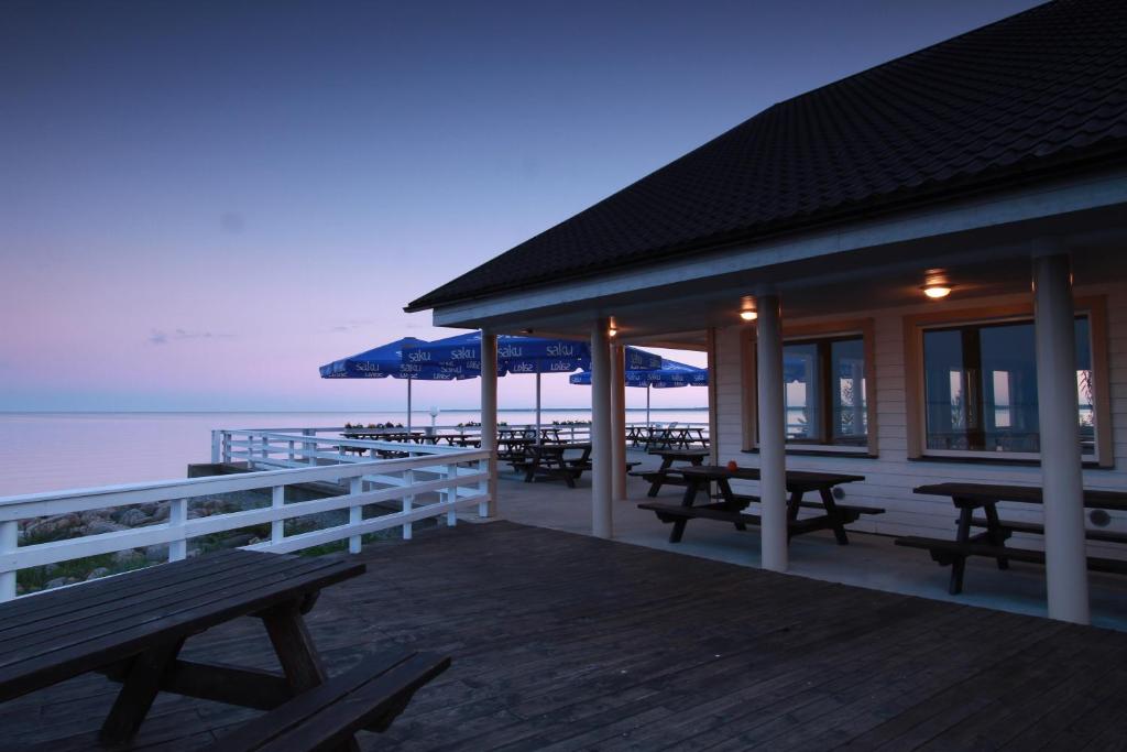 Valgeranna朵贝拉尼蓝娜玛佳酒店的海滩上带野餐桌和遮阳伞的建筑
