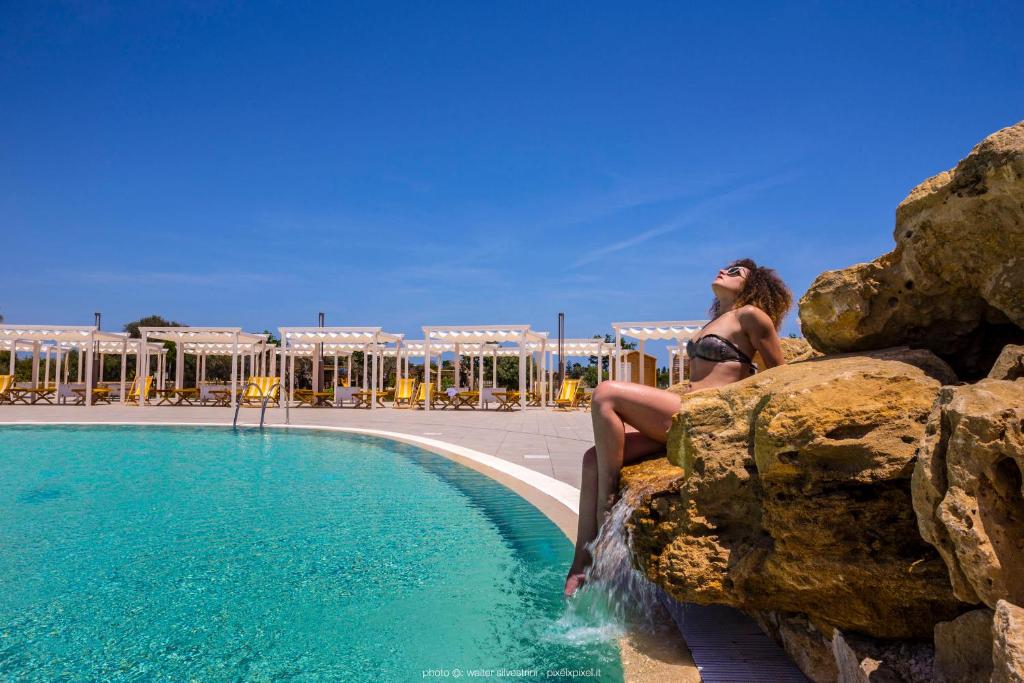 锡拉库扎Hotel Casale Milocca的坐在游泳池旁的岩石上的女人