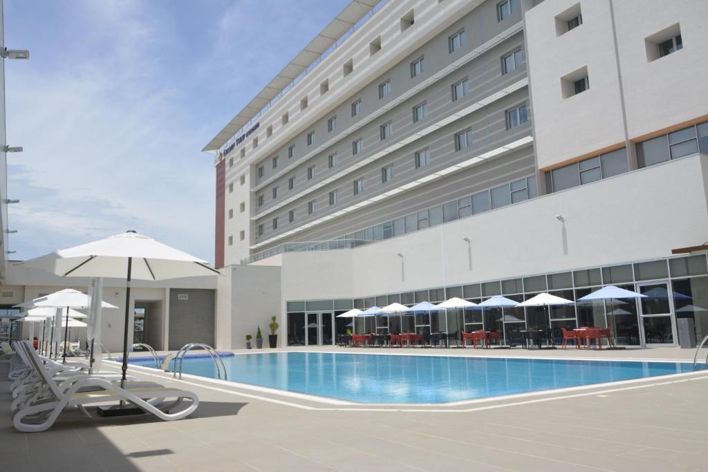 科托努迪帕美特金郁金香酒店的酒店大楼前的游泳池配有椅子和遮阳伞