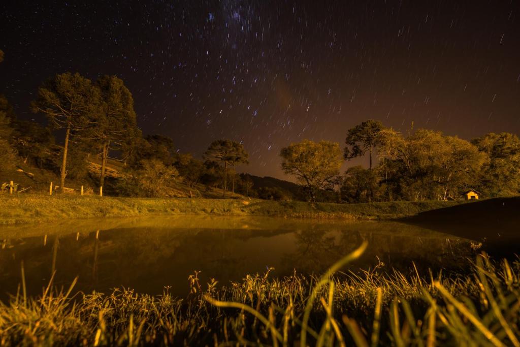 乌鲁比西Pousada Recanto da Serra - Unidade Campestre的在一个田野的池塘上度过的星空之夜