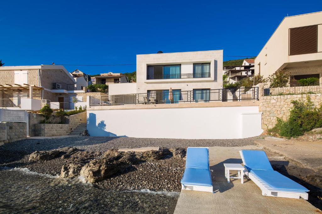 蒂瓦特Villa Krasici的两把蓝色躺椅在房子前面的海滩上