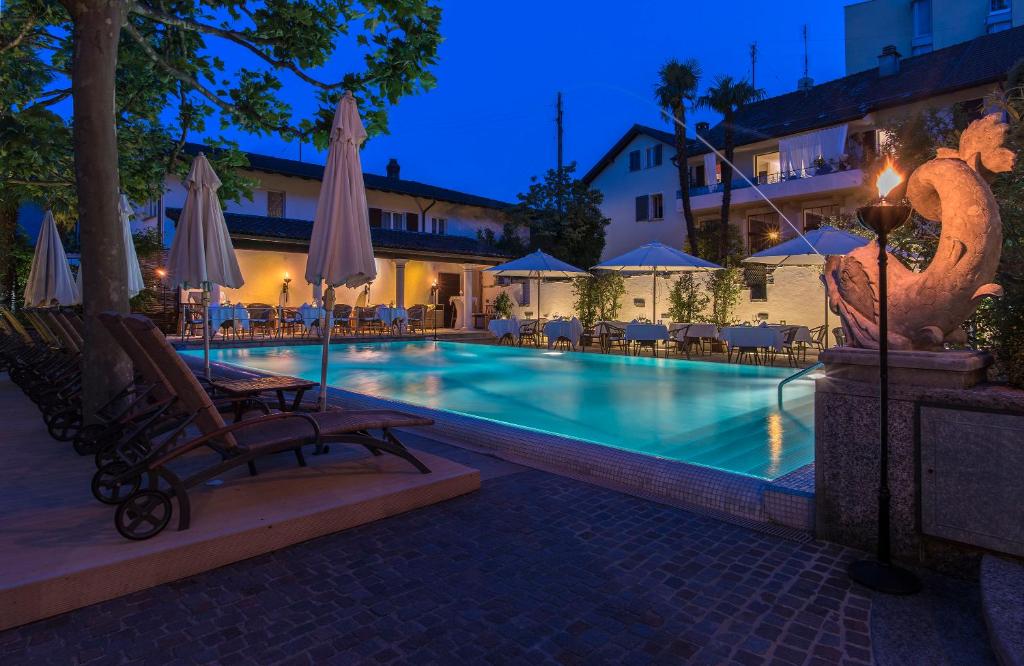 布里萨戈Suiten-Hotel Sunstar Brissago的游泳池在晚上提供椅子和遮阳伞