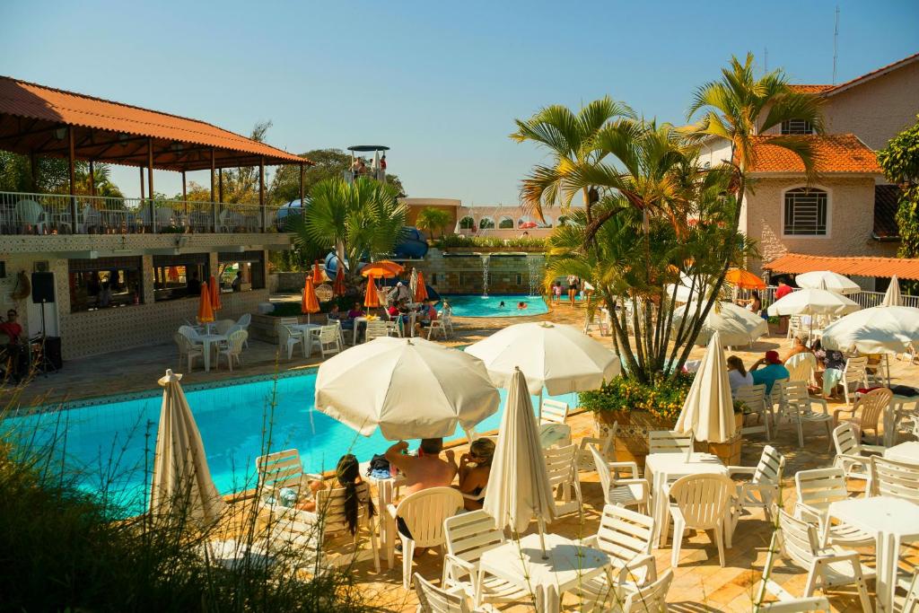 圣代佩德罗Hotel Fazenda Fonte Colina Verde的一组桌椅,在游泳池旁边配有遮阳伞