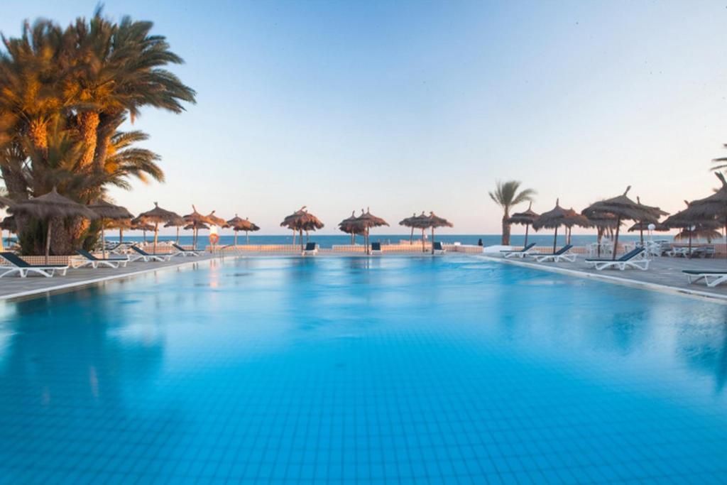 米多恩El Mouradi Djerba Menzel的海滩上带椅子和遮阳伞的大型游泳池