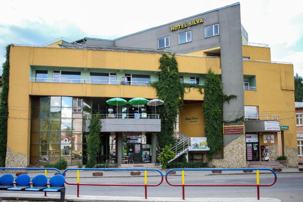 瓦特拉多尔内Hotel Silva的前面有桌子和遮阳伞的黄色建筑