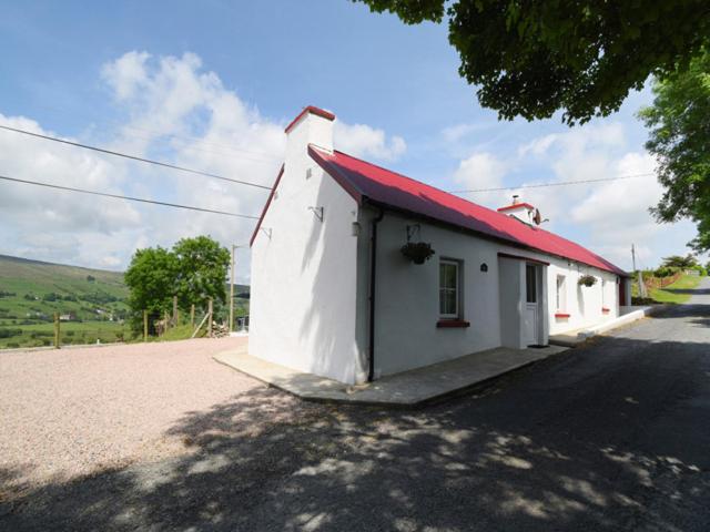 CommeenKerrigan's Cottage的一条白色的小建筑,在路上有红色的屋顶