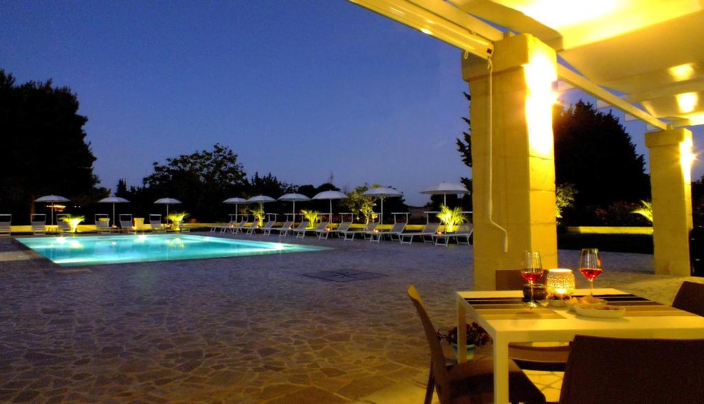 博尔加涅La Casina Di Borgagne的夜间带桌子和遮阳伞的游泳池
