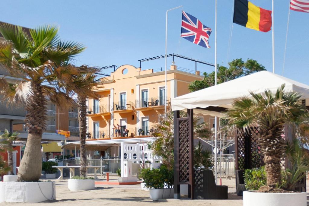 里米尼假日海滩酒店的两面旗帜在棕榈树建筑前飞