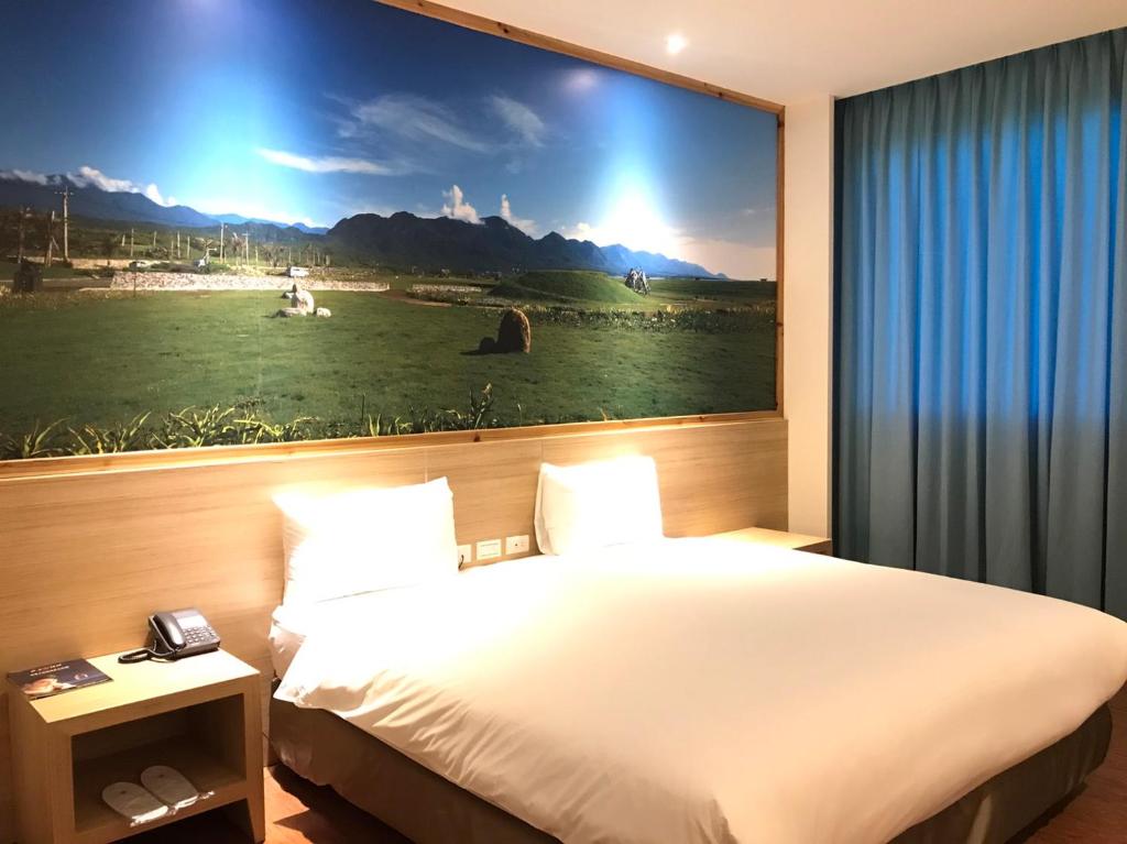 台东綺麗商旅園區館的酒店客房设有一张壁挂着大画的床铺。