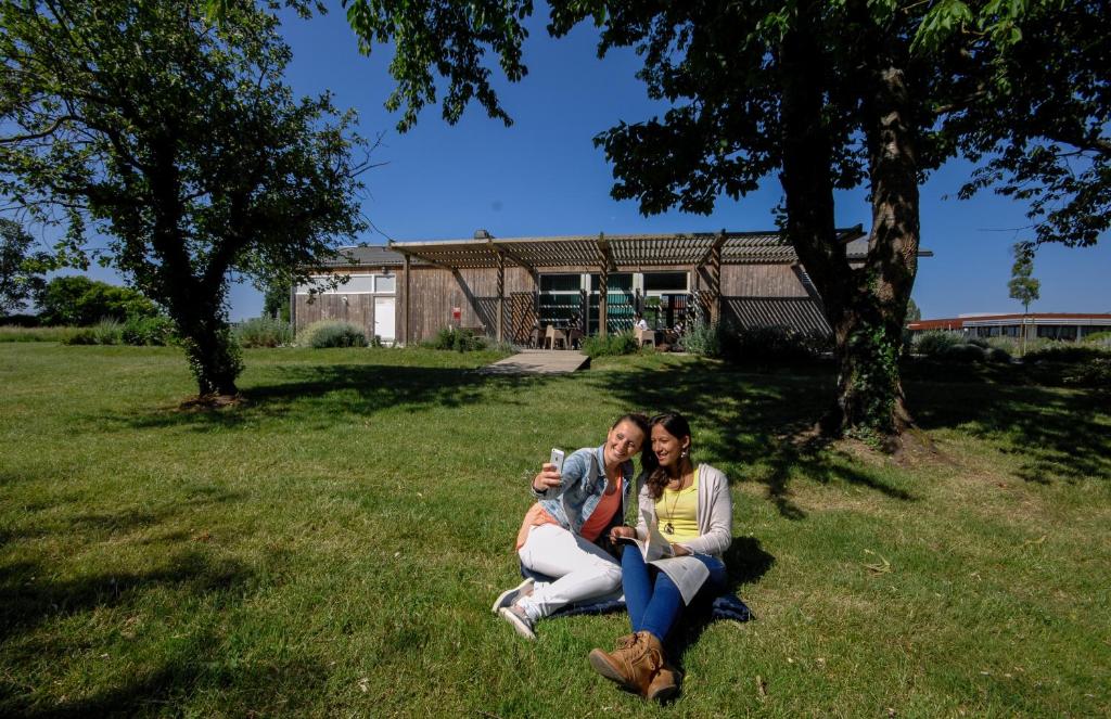 罗什福尔Auberge de jeunesse Rochefort的两个女人坐在草地上,拿着照相机