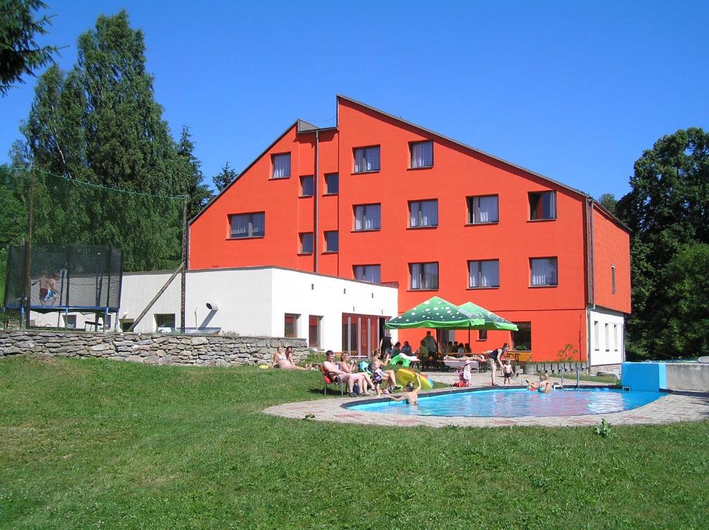 Pusté ŽibřidoviceHotel Na Trojce的一座红色的大建筑,人们坐在游泳池周围