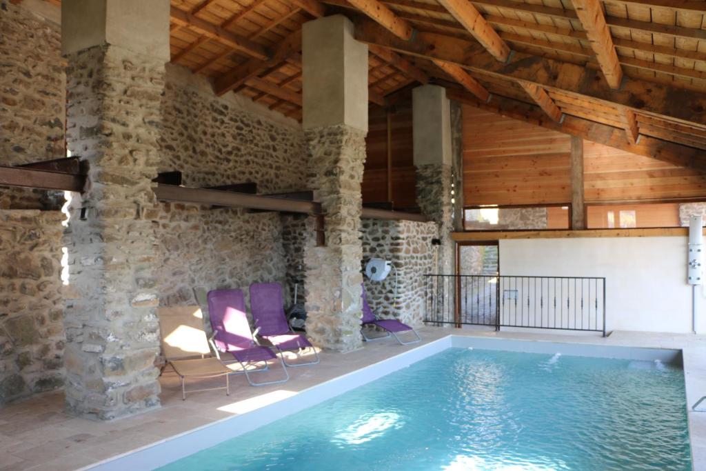 普里瓦Domaine de Chabanet的一个带石墙和木制天花板的房间的游泳池