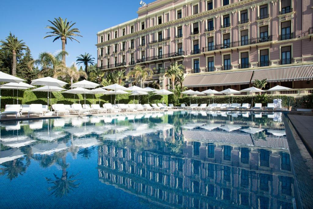 费拉角圣让Hotel Royal-Riviera的一座带遮阳伞的建筑前的游泳池
