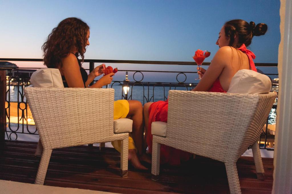 干尼亚Chania Inn的两个女人坐在阳台上的椅子上,阳台上有玫瑰