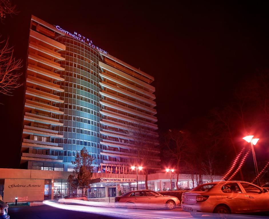 阿拉德阿拉德大陆酒店的一座高高的建筑,晚上有汽车停在停车场