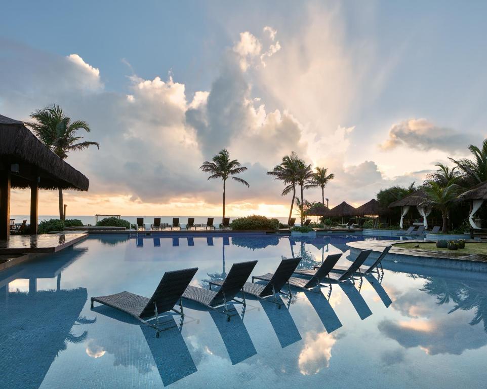 特赖里琐拉海滩酒店 的一个带椅子和棕榈树的游泳池,日落