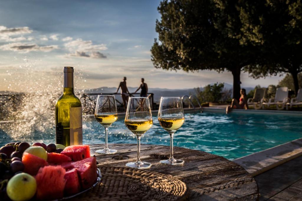 托尔贾诺Il Poggio Delle Ginestre的游泳池畔桌子上放着三杯葡萄酒和水果