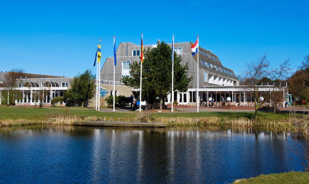 霍勒姆Fletcher Hotel-Restaurant Amelander Kaap的一座大建筑,在湖前有旗帜