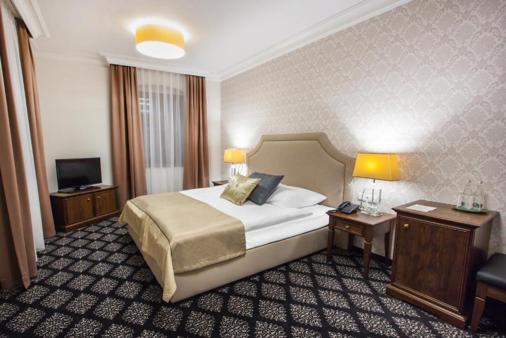 ToszekHG Hotel的酒店客房设有床、两张桌子和一台电视