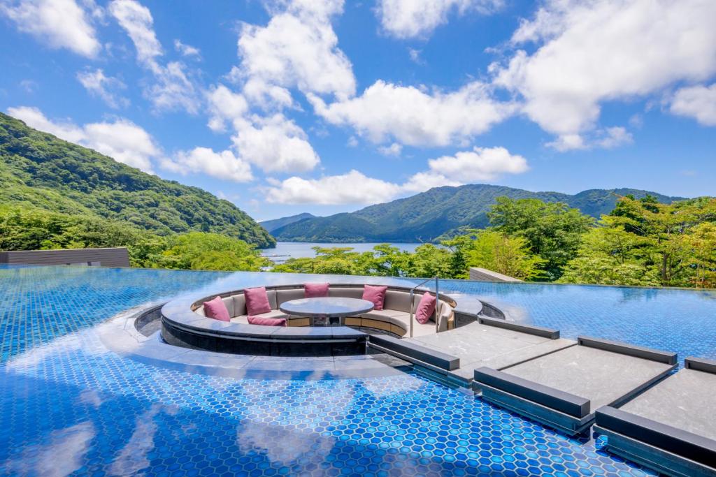 箱根箱根芦之湖花织旅馆(Hakone Ashinoko Hanaori)的一个带桌椅和山脉的无边泳池