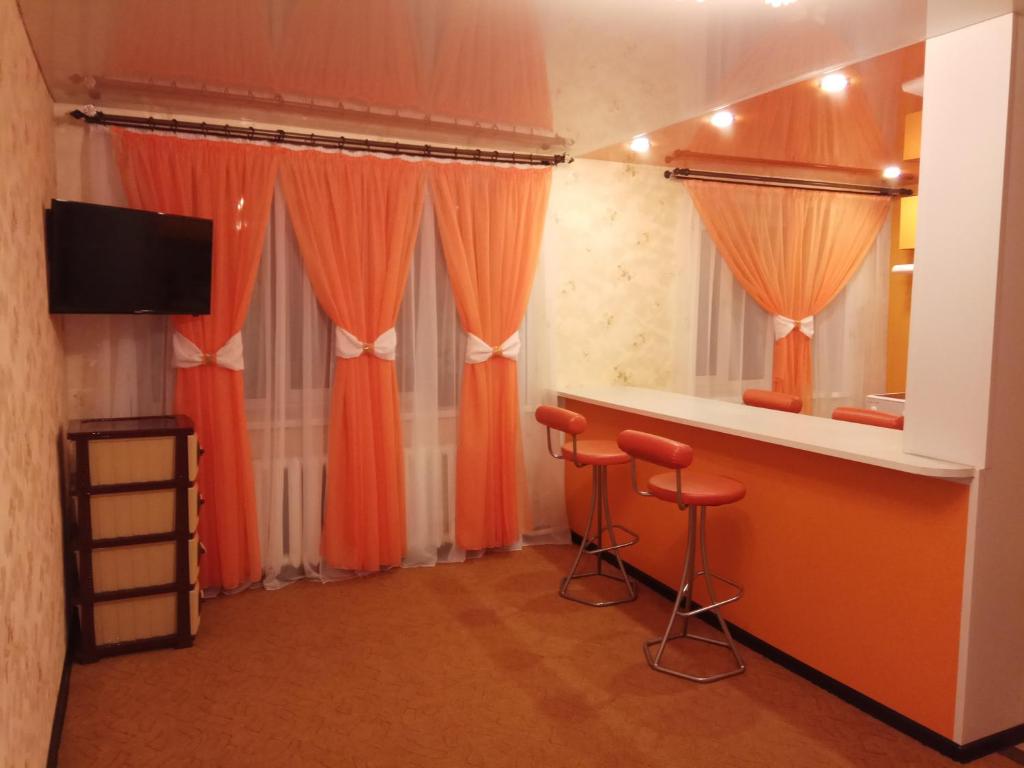诺里尔斯克Leninskiy Prospekt 25的一间设有橙色窗帘和两个酒吧凳的房间