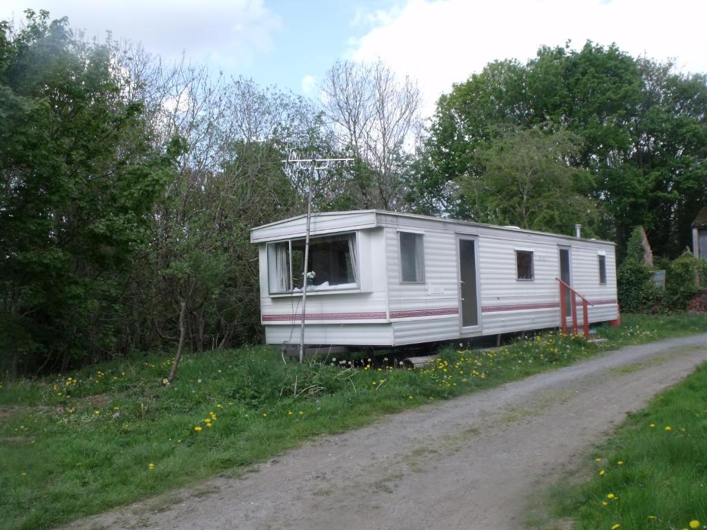 巴拉caravan nestled away amongst trees on edge of farm yard的停在土路一侧的白色拖车