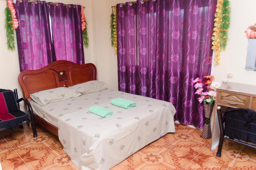 奥隆阿波朱丽斯热带公寓的一间卧室配有紫色窗帘和一张带两条毛巾的床