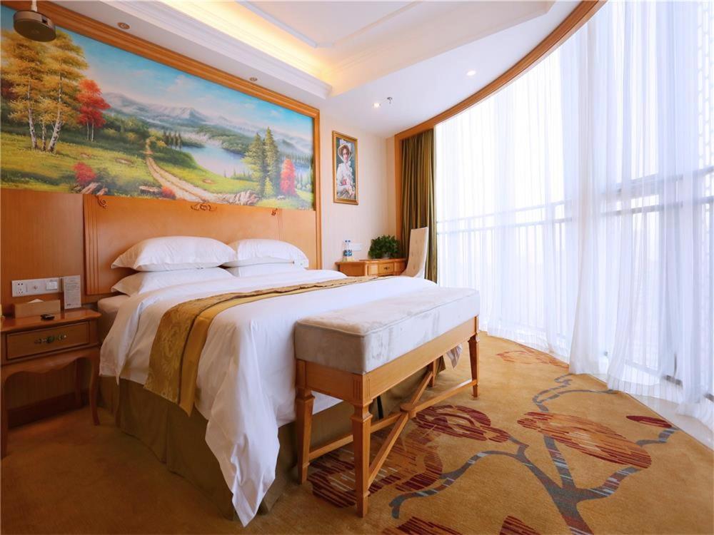 烟台维也纳国际酒店山东烟台长江路星颐广场店的卧室配有一张大床,墙上挂有绘画作品