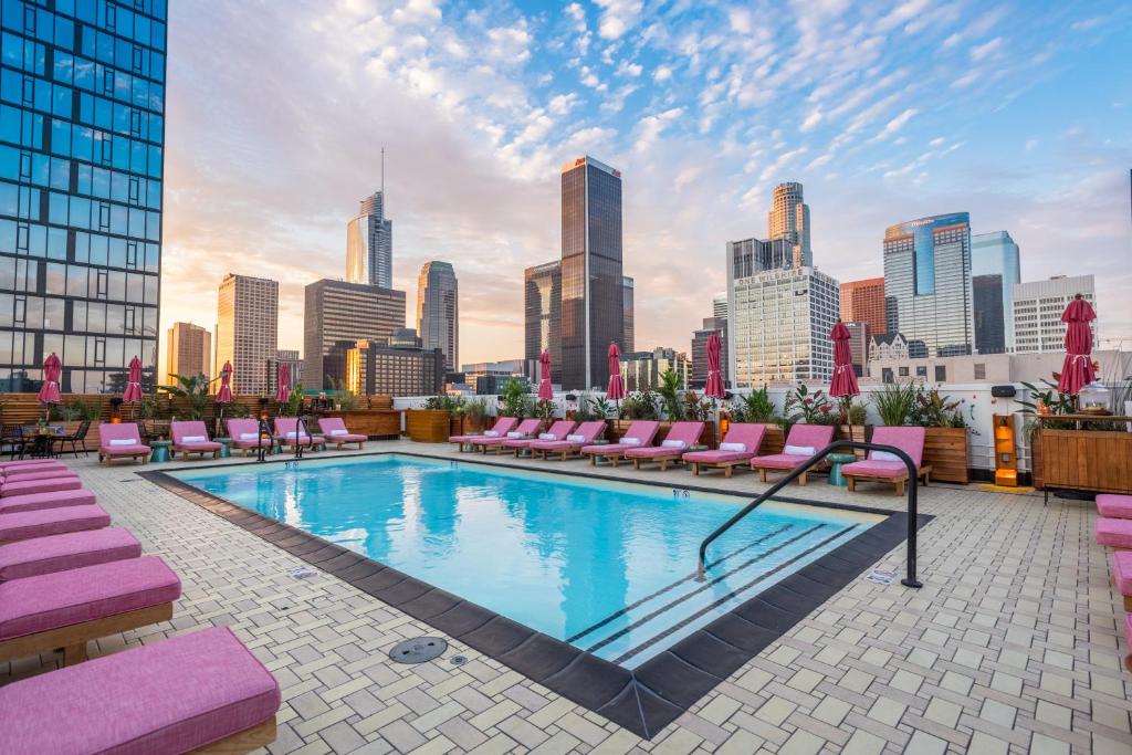 洛杉矶Freehand Los Angeles的一个带粉红色躺椅的屋顶游泳池和城市天际线