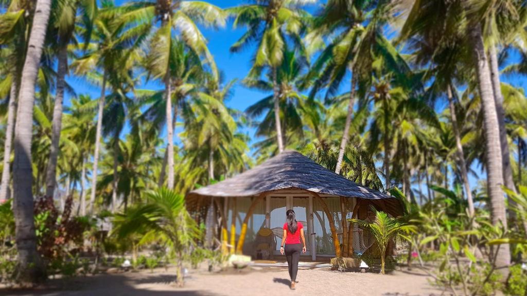 毛梅雷椰子园海滩度假村 的走在棕榈树前的小小屋的女人