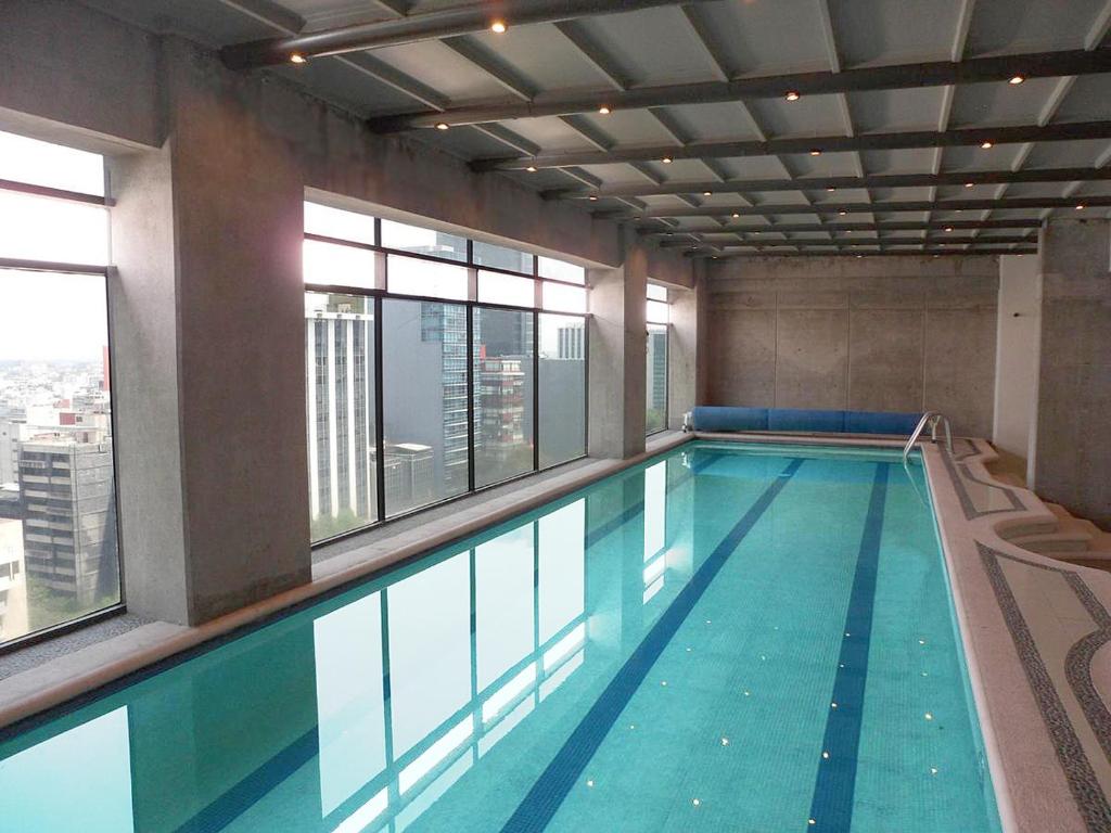 墨西哥城卡普里瑞芙尔玛410号公寓式酒店的一座大型游泳池,位于一座带窗户的建筑内