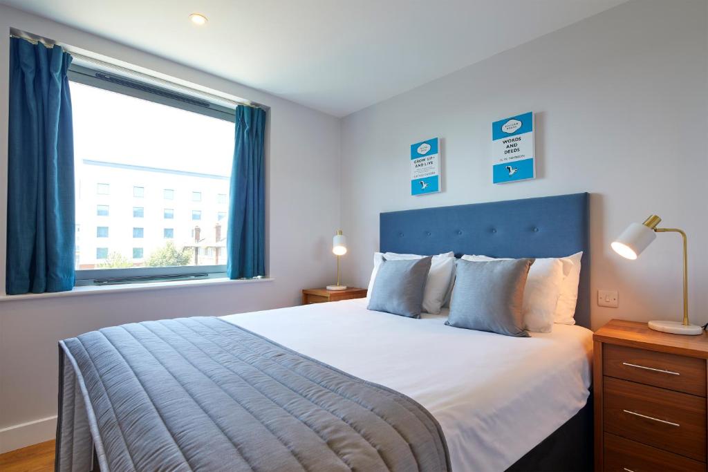 法恩伯勒HQ Aparthotel Farnborough的一间卧室配有一张带蓝色床头板的床和窗户