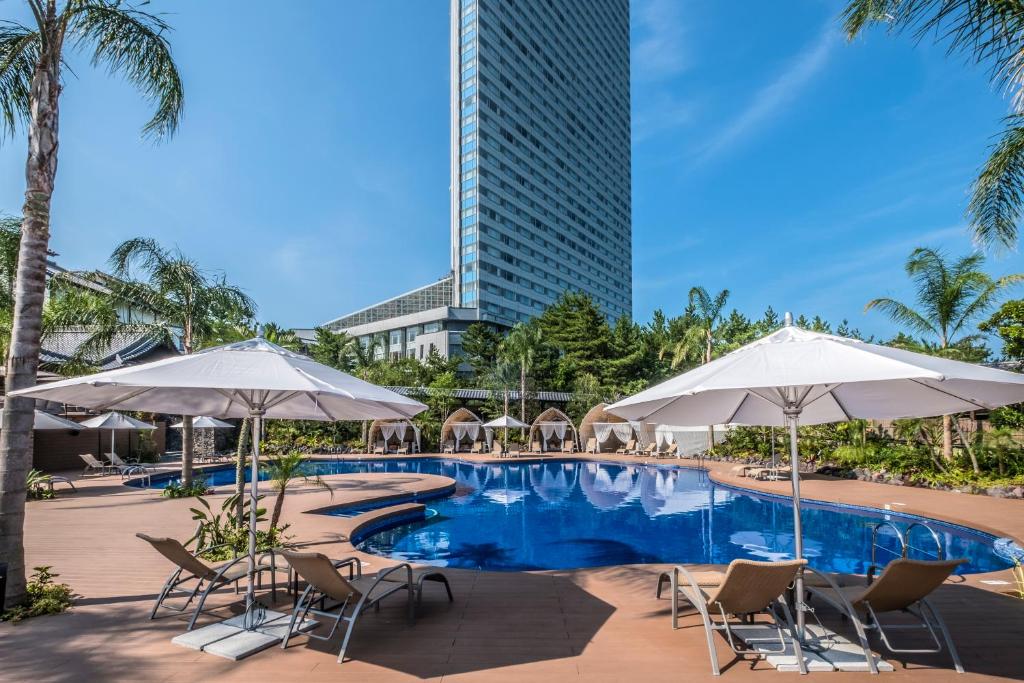 宫崎喜来登顶级海洋度假酒店的一个带椅子和遮阳伞的游泳池和一座高大的建筑
