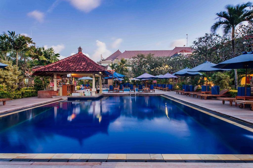 库塔Kuta Puri Bungalows, Villas and Resort的度假村的游泳池,配有桌子和遮阳伞