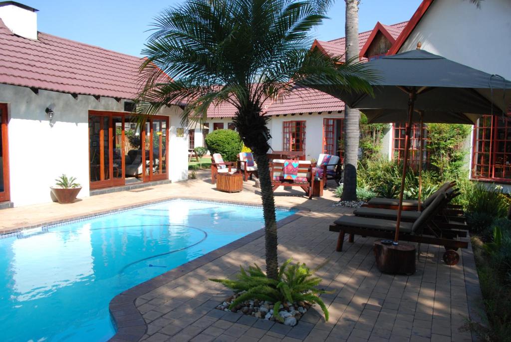 肯普顿帕克Journey's Inn Africa Airport Lodge的一座房子旁的游泳池,里面种着棕榈树
