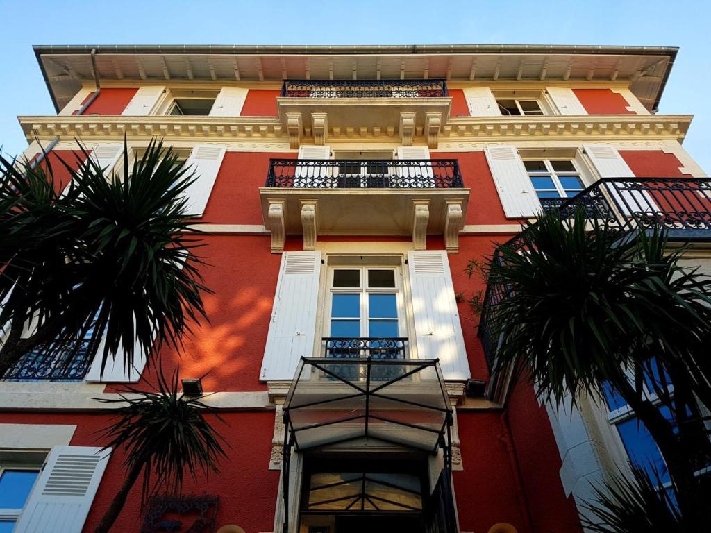 比亚里茨Hôtel & Espace Bien-être La Maison du Lierre的一座高大的红色建筑,前面有棕榈树