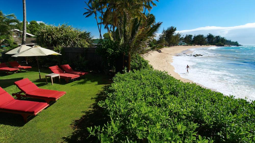 帕依亚Paia Inn的海滩上设有红色椅子和遮阳伞,大海