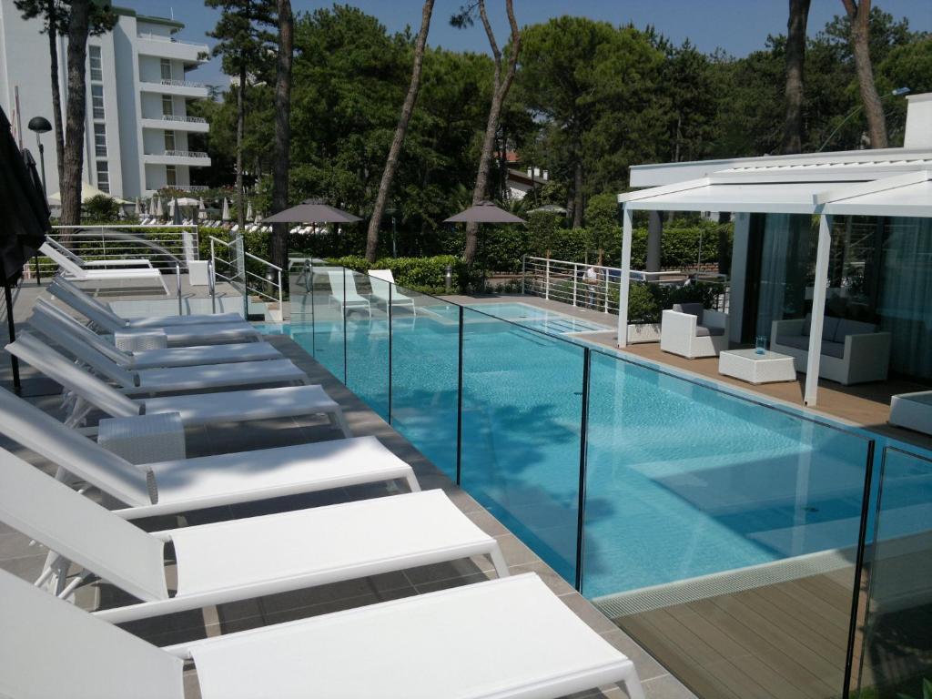 利尼亚诺萨比亚多罗Suite Erica Lignano Hotel的一座带白色躺椅的游泳池,位于大楼旁