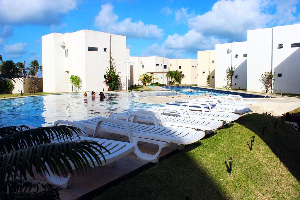 马拉卡贾Paraiso de Maracajau 4的一座大楼前的游泳池,配有白色躺椅