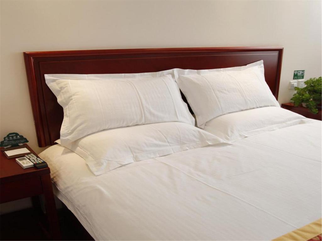 上海格林豪泰上海中山沪太商务酒店的白色的床、白色枕头和木制床头板