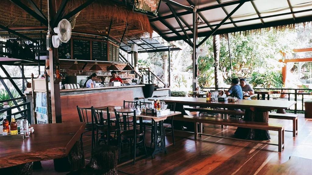 Amphoe Sawang Daen Din查塔帕雅度假村的一间带木桌椅的餐厅和一间酒吧