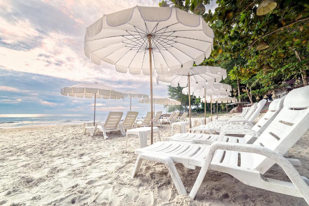 沙美岛Samed Villa Resort的海滩上的一组白色椅子和遮阳伞
