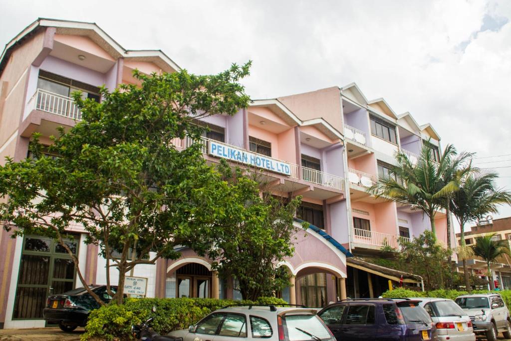 姆巴拉拉Pelikan Hotel的一座粉红色的建筑,前面有汽车停放