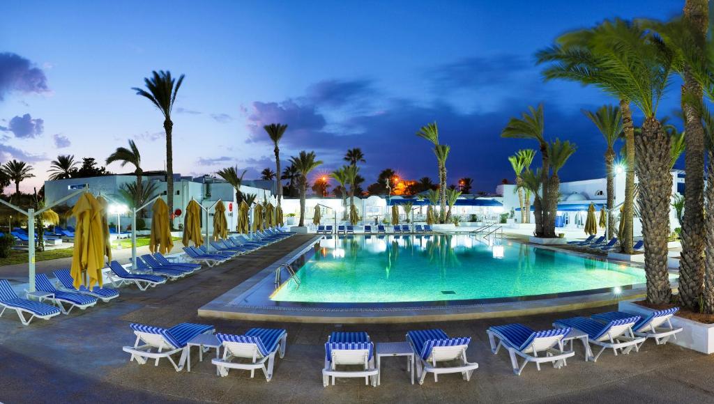 阿格希尔Hari Club Beach Resort的游泳池在晚上设有椅子和棕榈树