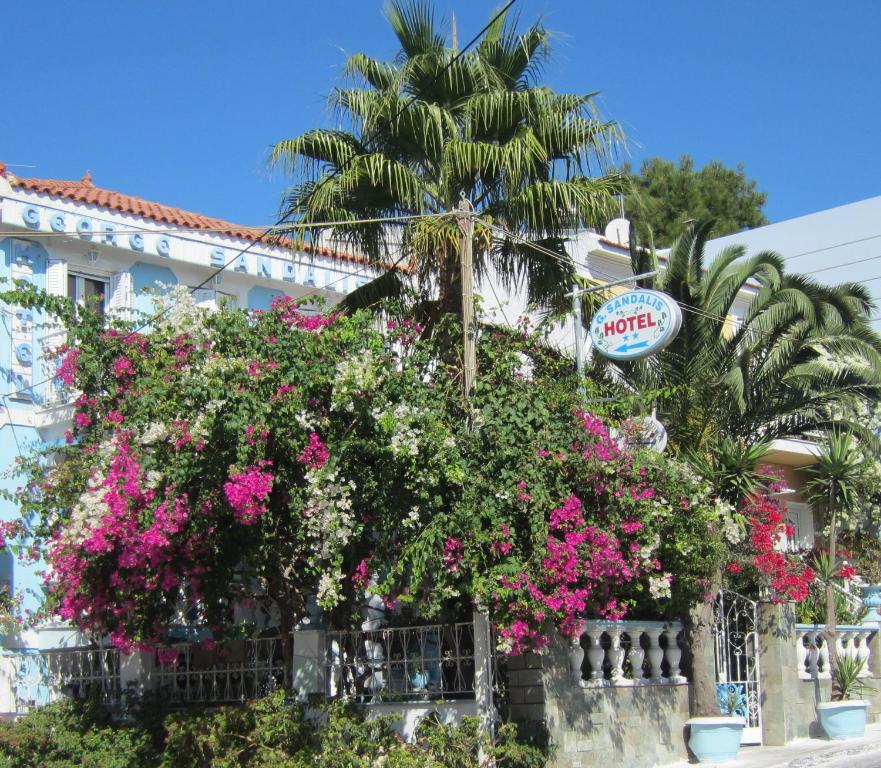 毕达哥利翁Sandalis Hotel的一座有粉红色花朵和棕榈树的建筑