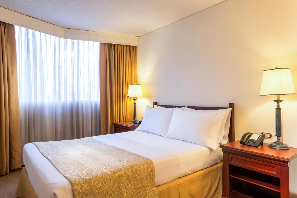 波哥大丹恩AV.19酒店的一间酒店客房,配有一张床铺和一张桌子上的电话