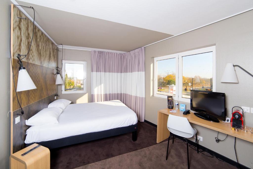 图卢兹Ibis Toulouse Purpan Aeroport的酒店客房配有一张床和一张书桌及一台电视