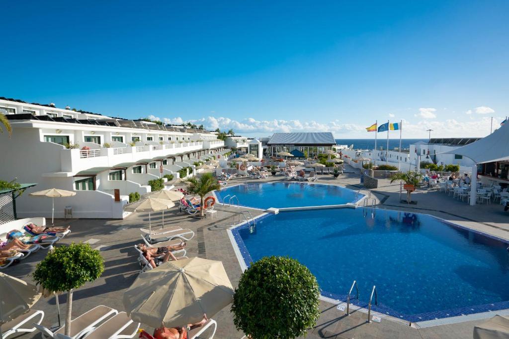 卡门港Relaxia Lanzaplaya的酒店设有带椅子和遮阳伞的游泳池